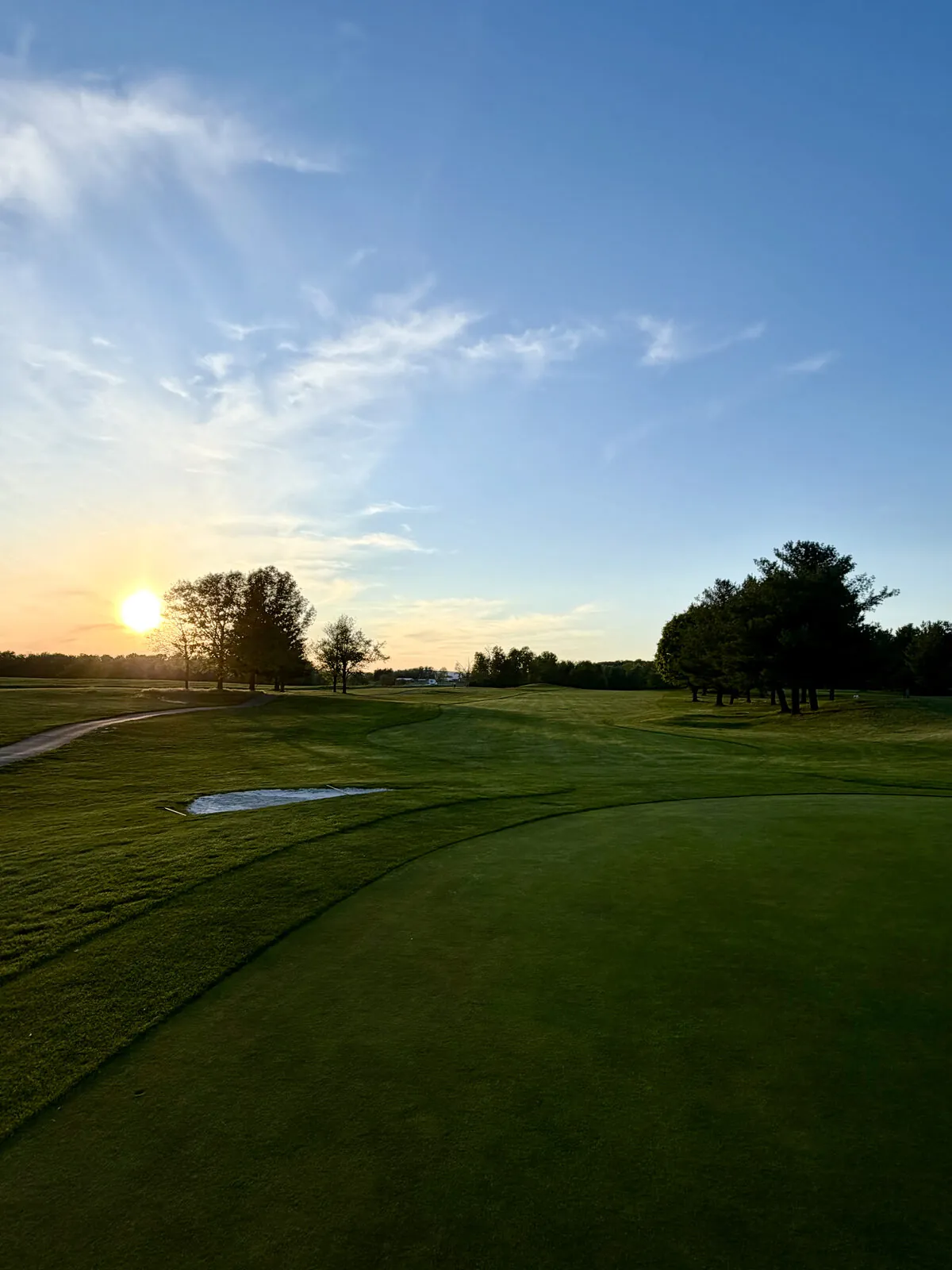 Low sun sinking behind trees along a quiet golf course fairway on a clear spring evening