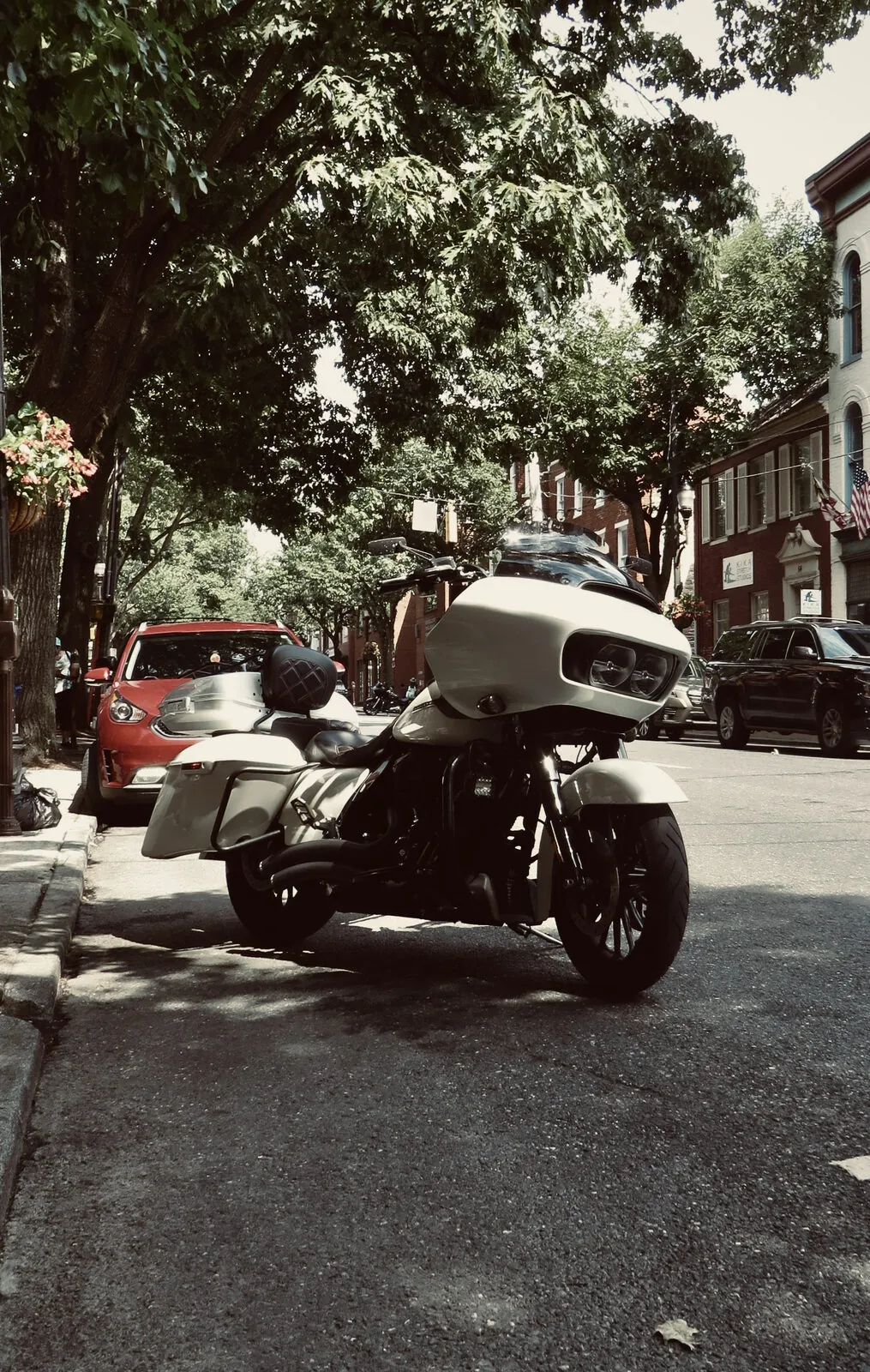 Muted-tone Harley touring motorcycle parked along a tree-shaded historic downtown street in summer