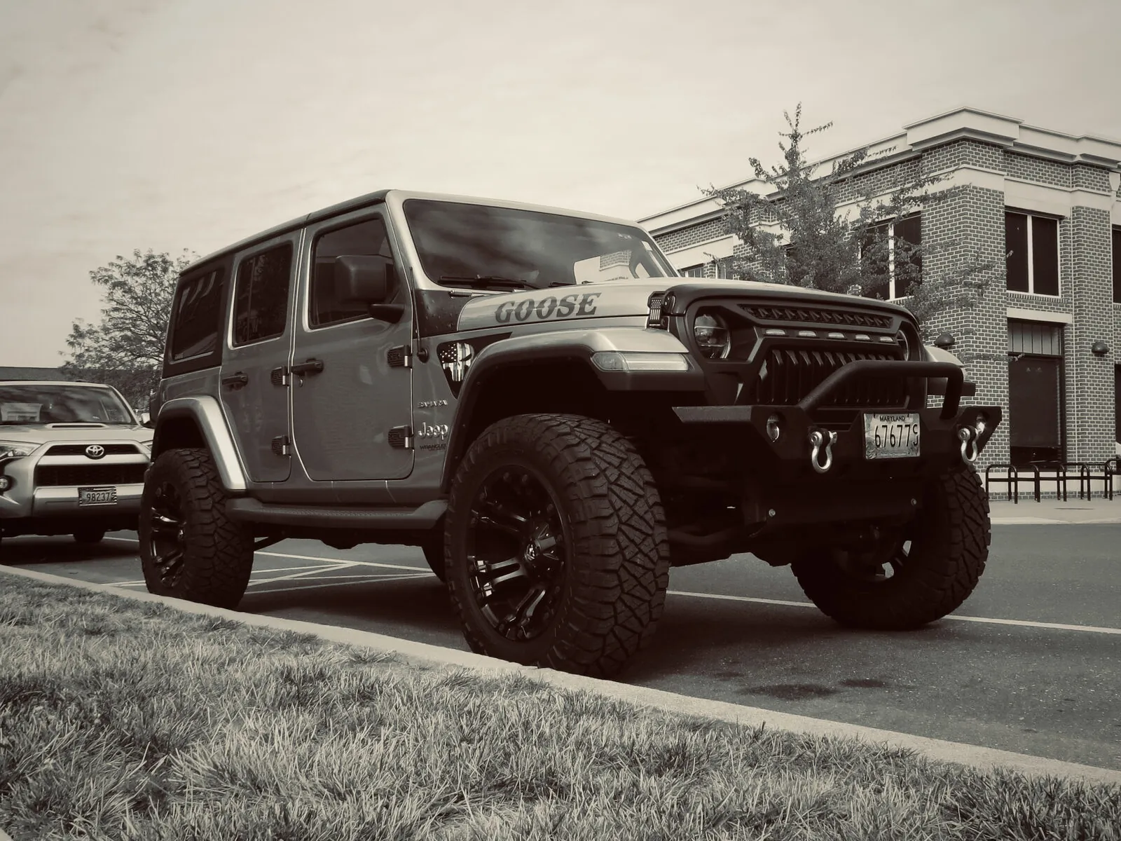Sepia-toned lifted Jeep Wrangler nicknamed 'Goose' parked beside a brick building