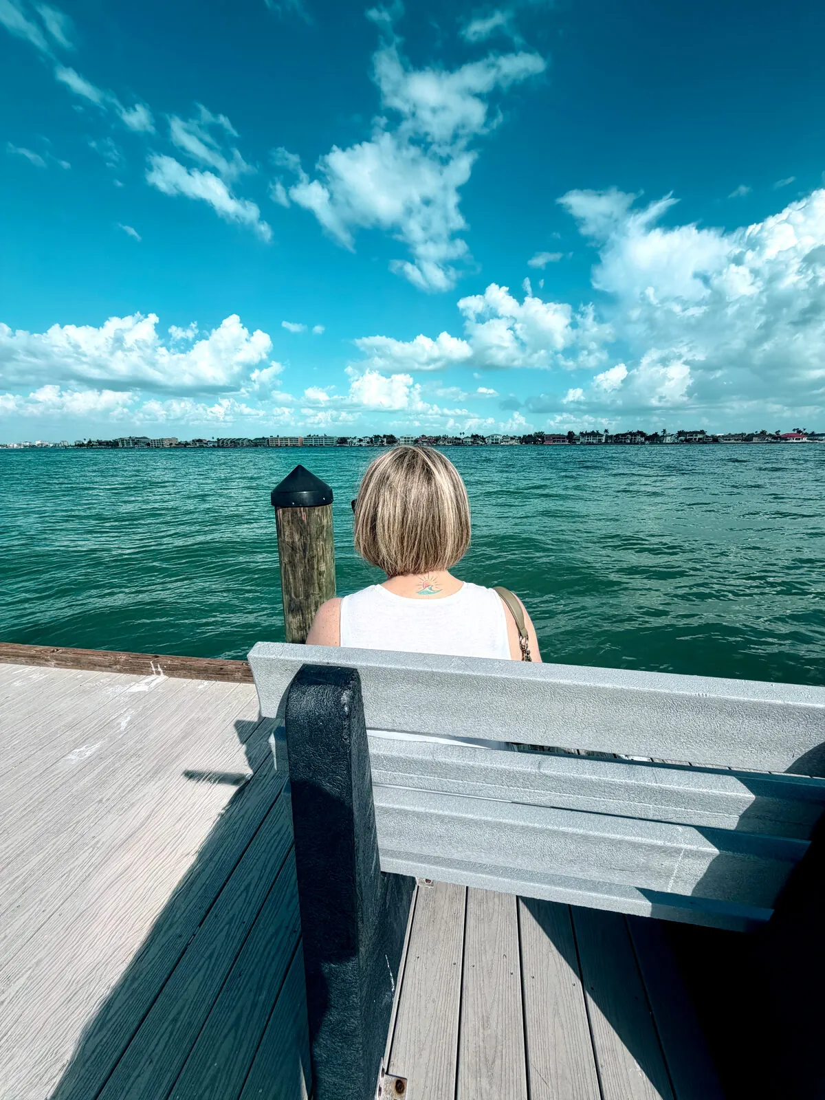A woman sitting on a dock bench looking out over bright turquoise coastal water