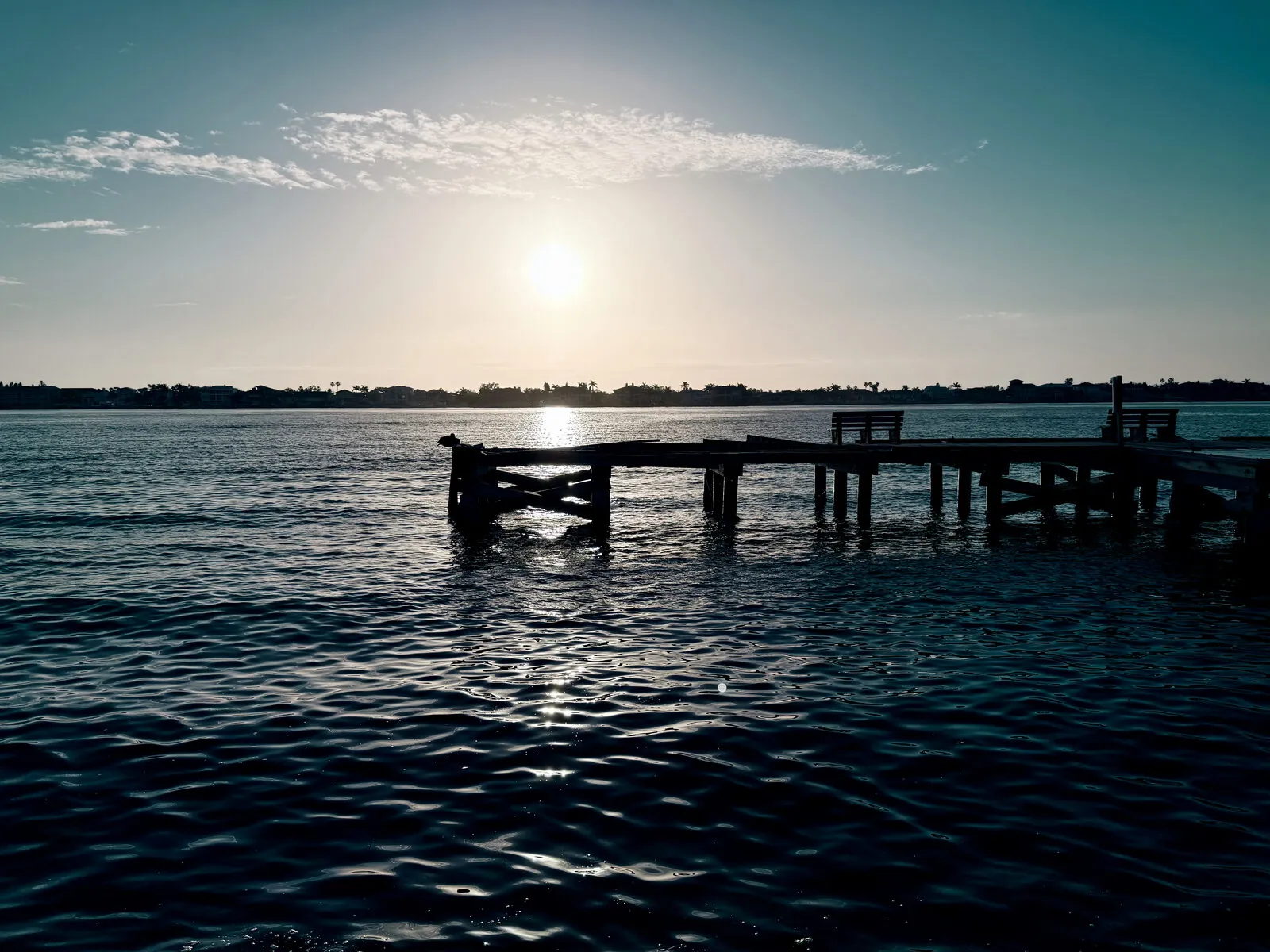 A weathered pier silhouetted against a low sun over calm water