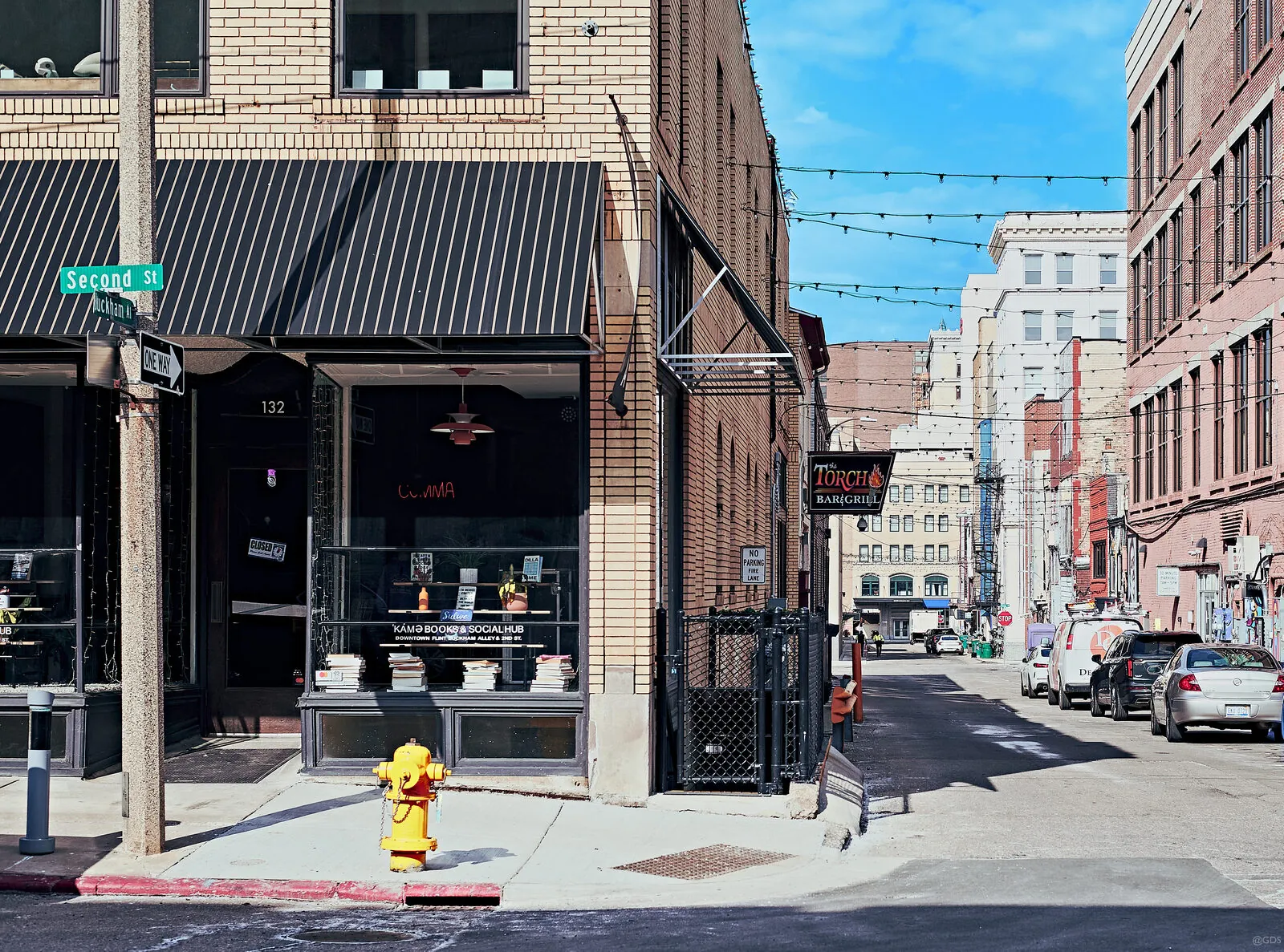 A downtown Flint street corner on a clear day — storefront awnings and a yellow hydrant, the avenue receding toward taller buildings