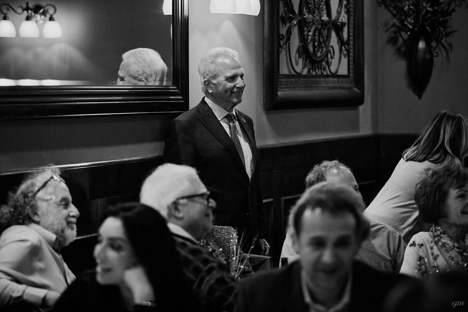Black-and-white candid — a candidate standing among guests at an evening reception
