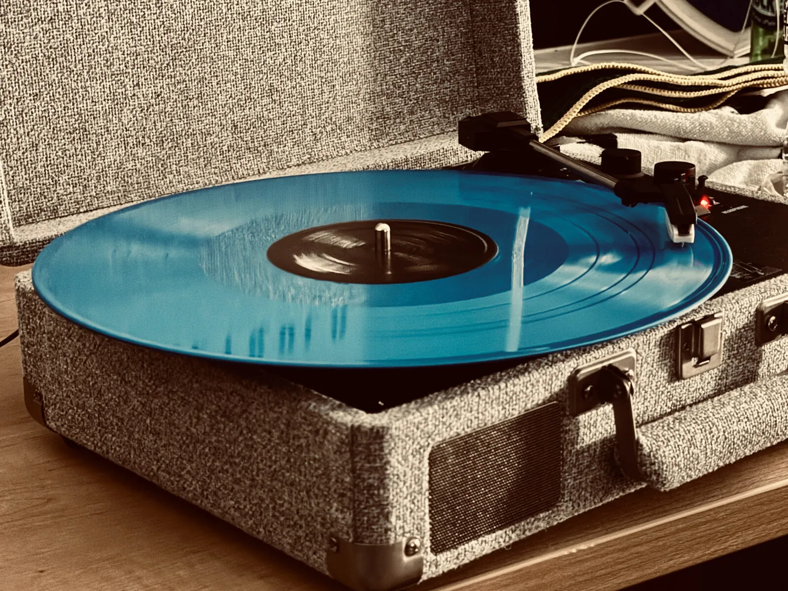 A blue vinyl record spinning on a portable turntable in warm light