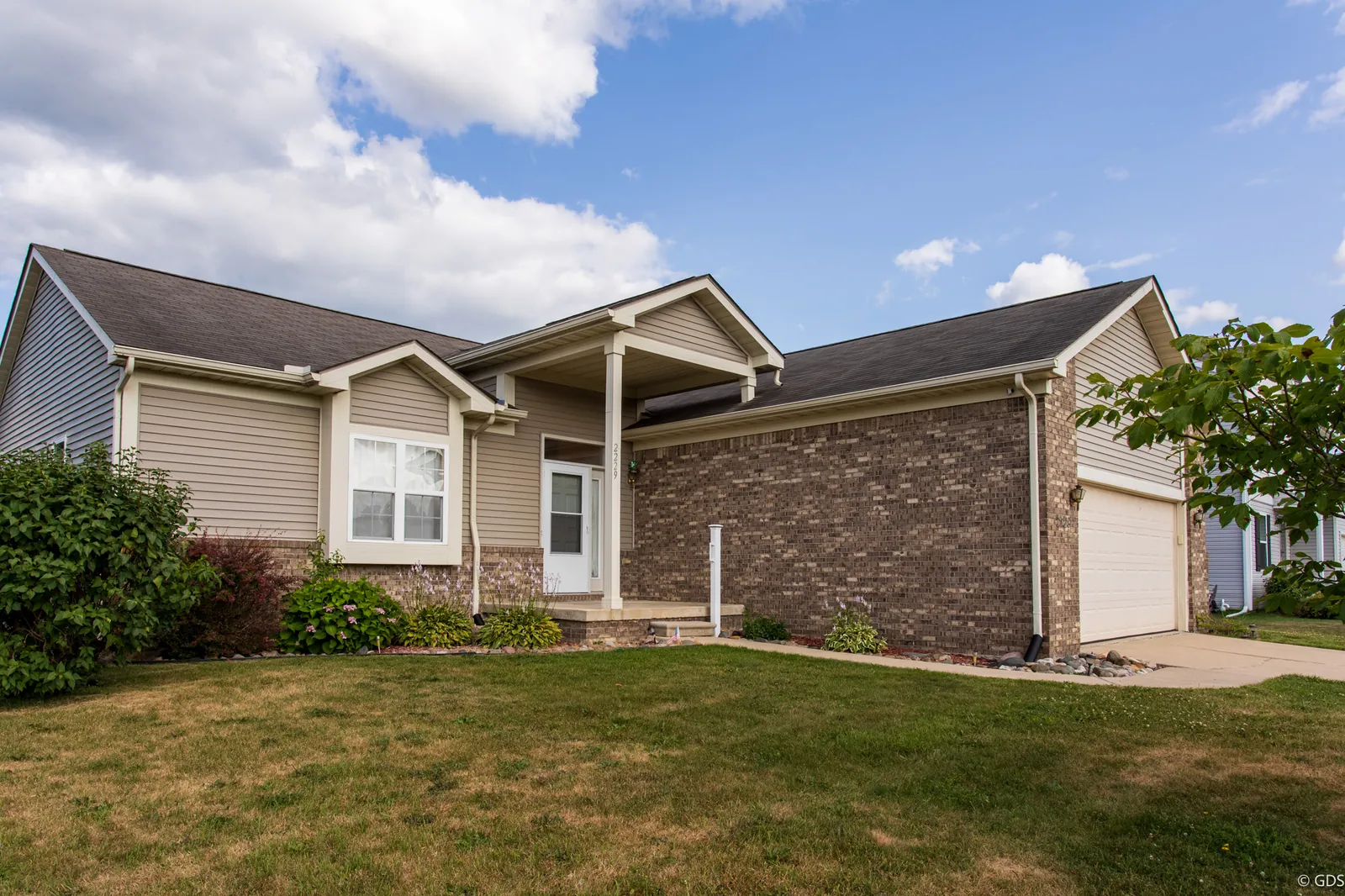 Brick-and-siding ranch with covered entry and two-car garage under summer clouds — 2229 Hunter Lane, Burton