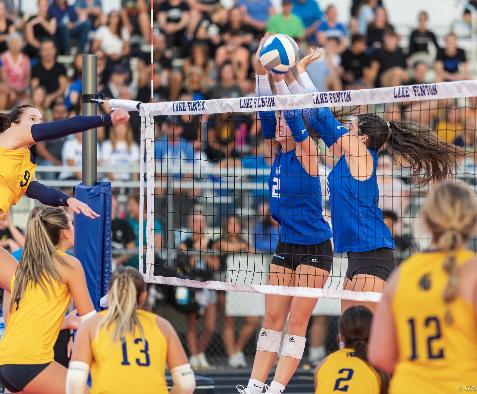 High school volleyball players meet at the net under the lights