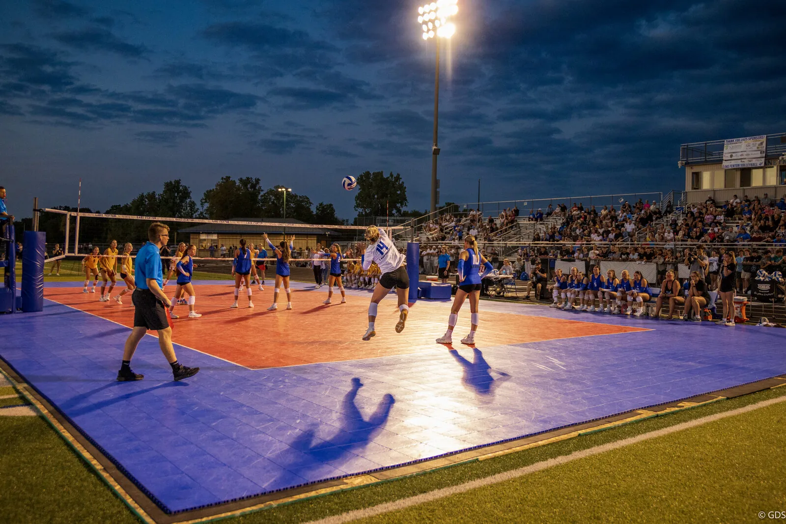 Outdoor night volleyball — a hitter rises for a spike as the stands look on