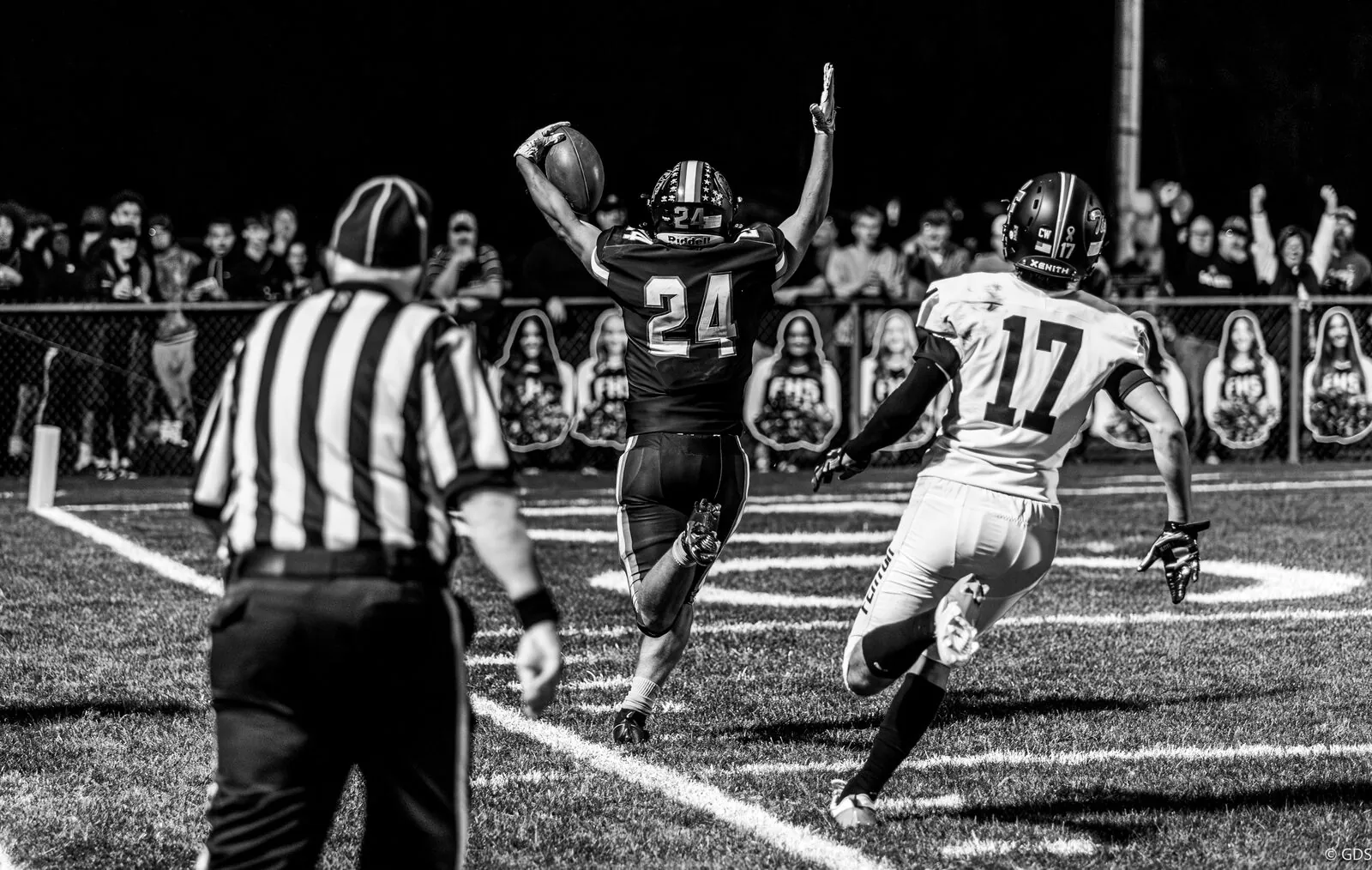 Black-and-white night football — a running back high-steps into the end zone past a defender, Flushing vs Fenton 2024